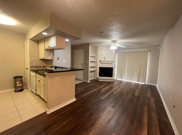 kitchen featuring a brick fireplace, light hardwood / wood-style flooring, kitchen peninsula, white dishwasher, and a textured ceiling