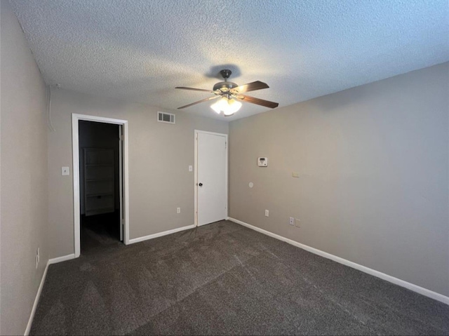 unfurnished bedroom featuring dark carpet, a textured ceiling, ceiling fan, a spacious closet, and a closet