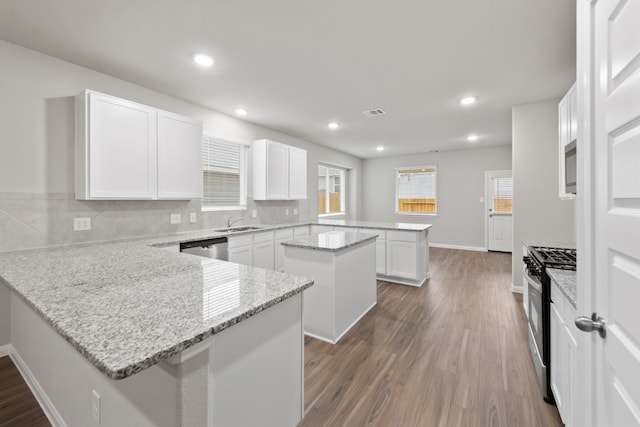 kitchen with kitchen peninsula, light stone counters, stainless steel appliances, white cabinets, and a center island