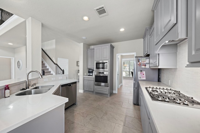 kitchen with appliances with stainless steel finishes, gray cabinets, tasteful backsplash, and sink