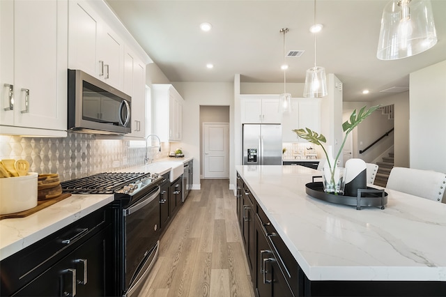 kitchen featuring stainless steel appliances, white cabinets, light hardwood / wood-style floors, a kitchen island, and hanging light fixtures