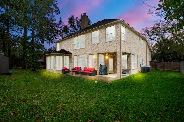 back house at dusk featuring a lawn, a patio area, and central air condition unit