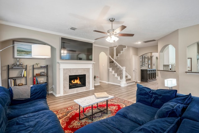 living room featuring a tile fireplace, light wood-type flooring, ceiling fan, and crown molding