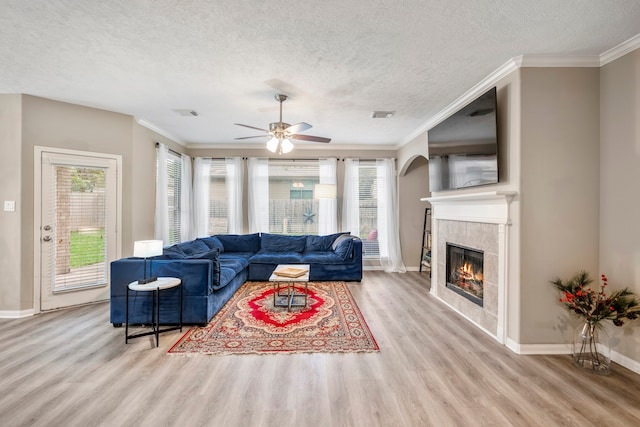 living room with light wood-type flooring, ornamental molding, a textured ceiling, ceiling fan, and a tile fireplace