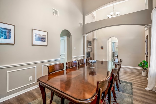 dining space with a high ceiling, ornate columns, a notable chandelier, and wood-type flooring