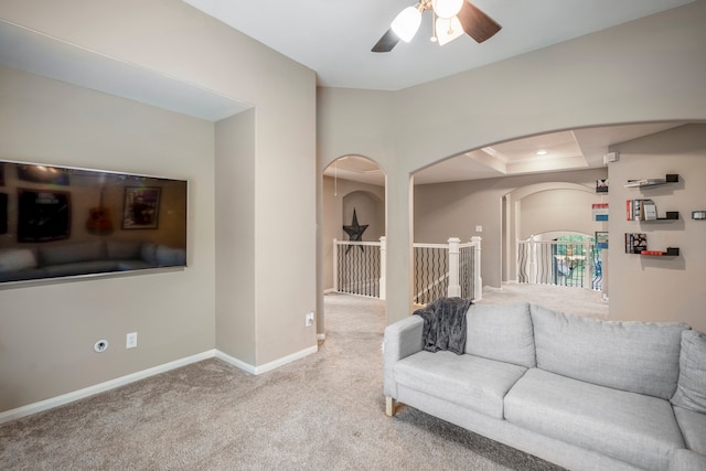 living room with a raised ceiling, ceiling fan, and carpet floors