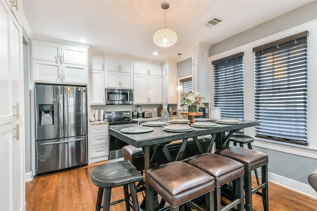 kitchen featuring dark wood-type flooring, stainless steel appliances, pendant lighting, a kitchen bar, and white cabinets