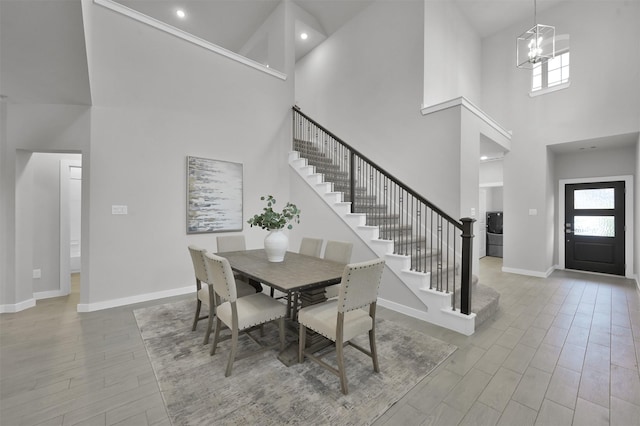 dining area with an inviting chandelier, a towering ceiling, and light wood-type flooring