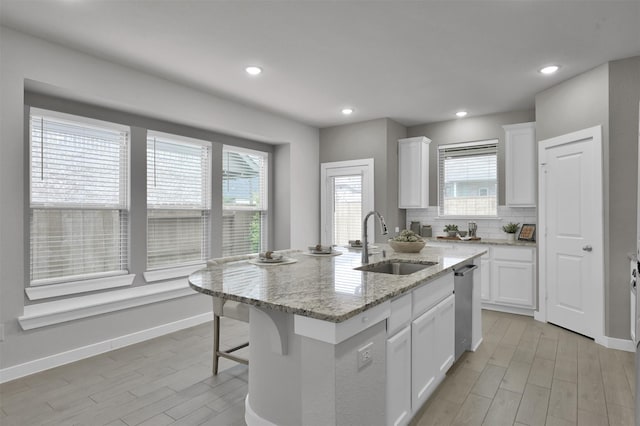 kitchen featuring light stone counters, sink, white cabinets, and a center island with sink