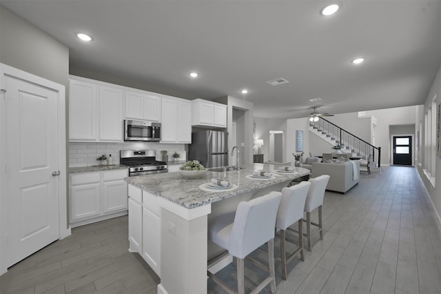 kitchen with light stone counters, an island with sink, a kitchen bar, white cabinetry, and stainless steel appliances