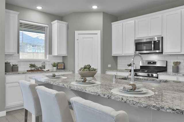 kitchen with white cabinets, light stone counters, stainless steel appliances, and tasteful backsplash