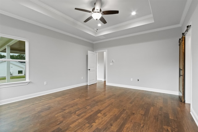 empty room with a barn door, dark hardwood / wood-style flooring, crown molding, and a tray ceiling