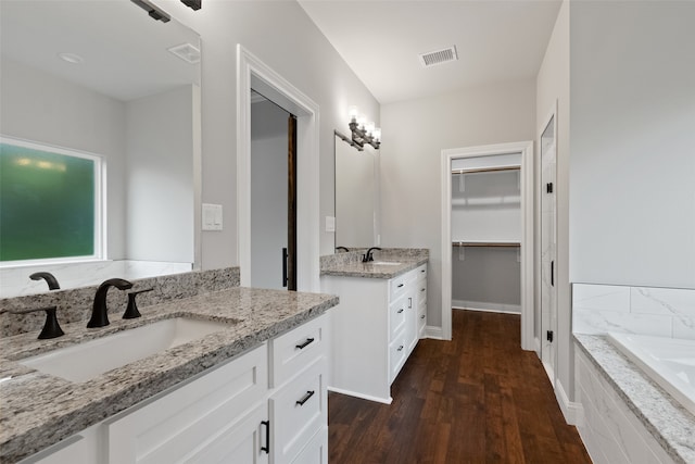 bathroom with wood-type flooring, vanity, and tiled bath