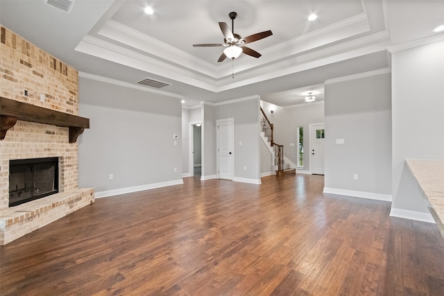 unfurnished living room with a raised ceiling, crown molding, dark hardwood / wood-style floors, ceiling fan, and a fireplace