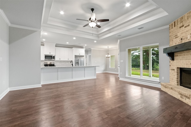 unfurnished living room featuring a fireplace, a tray ceiling, crown molding, and dark wood-type flooring