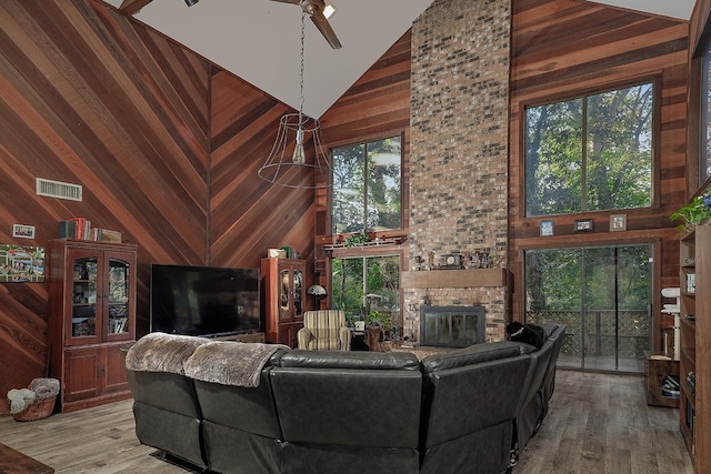 living room featuring a fireplace, light hardwood / wood-style flooring, high vaulted ceiling, and wood walls