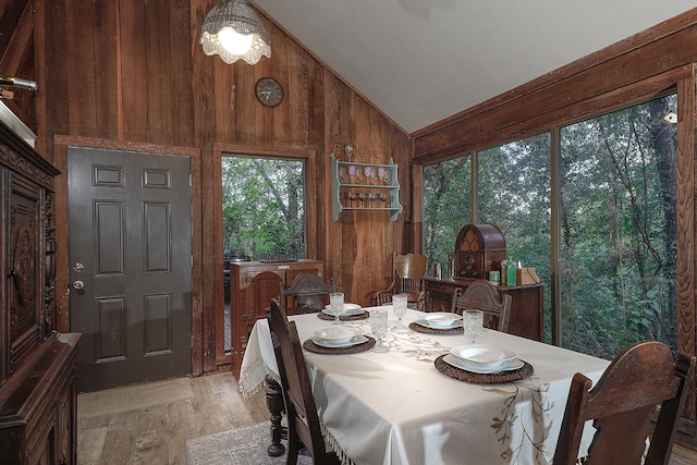 dining space with wood walls, light hardwood / wood-style floors, and high vaulted ceiling