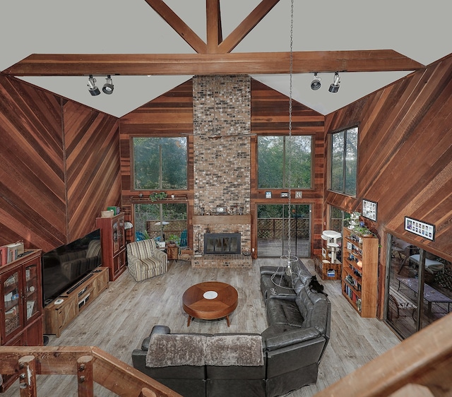 living room featuring light hardwood / wood-style flooring, high vaulted ceiling, beamed ceiling, wood walls, and a fireplace