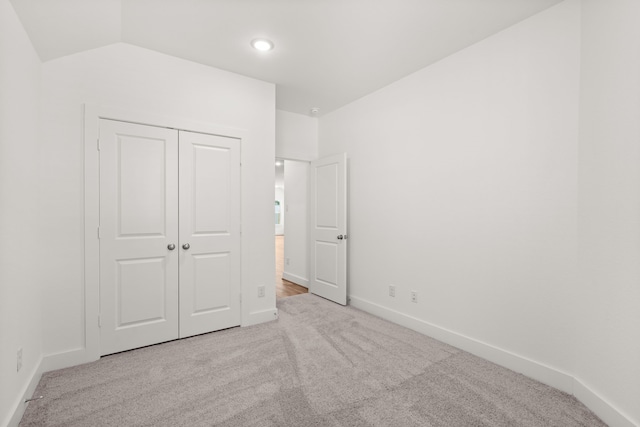 unfurnished bedroom with light colored carpet, a closet, and lofted ceiling