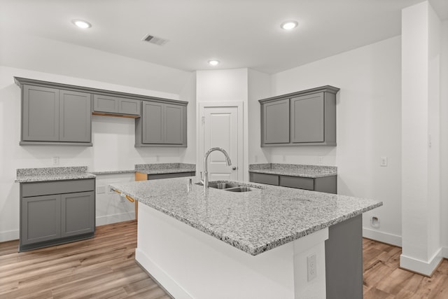 kitchen with light hardwood / wood-style floors, a kitchen island with sink, gray cabinetry, and sink