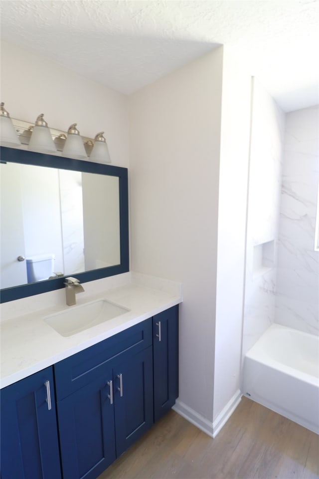 bathroom with a textured ceiling, vanity, hardwood / wood-style flooring, and tiled shower / bath