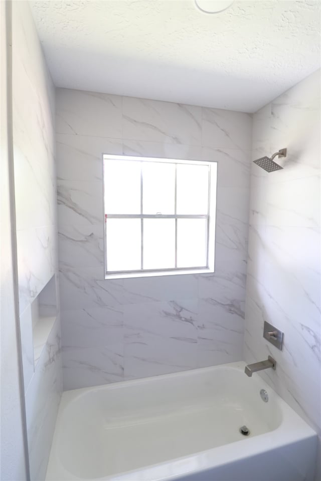 bathroom featuring a textured ceiling and tiled shower / bath