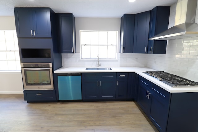 kitchen with light hardwood / wood-style flooring, stainless steel appliances, blue cabinets, and wall chimney range hood