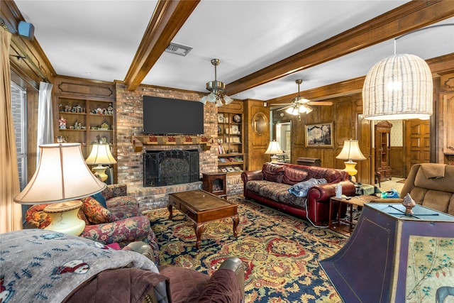 living room with beamed ceiling, a fireplace, ceiling fan, and wooden walls