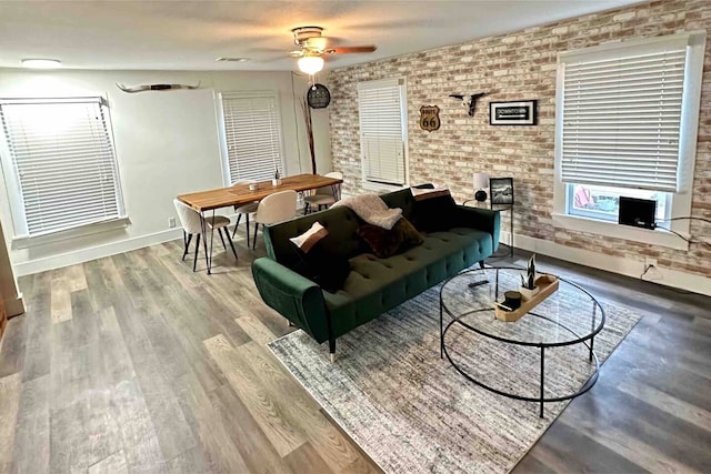 living room featuring hardwood / wood-style flooring, ceiling fan, and brick wall