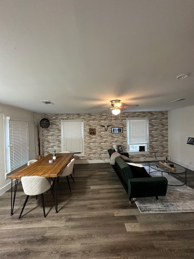 living room featuring dark hardwood / wood-style floors, ceiling fan, and brick wall