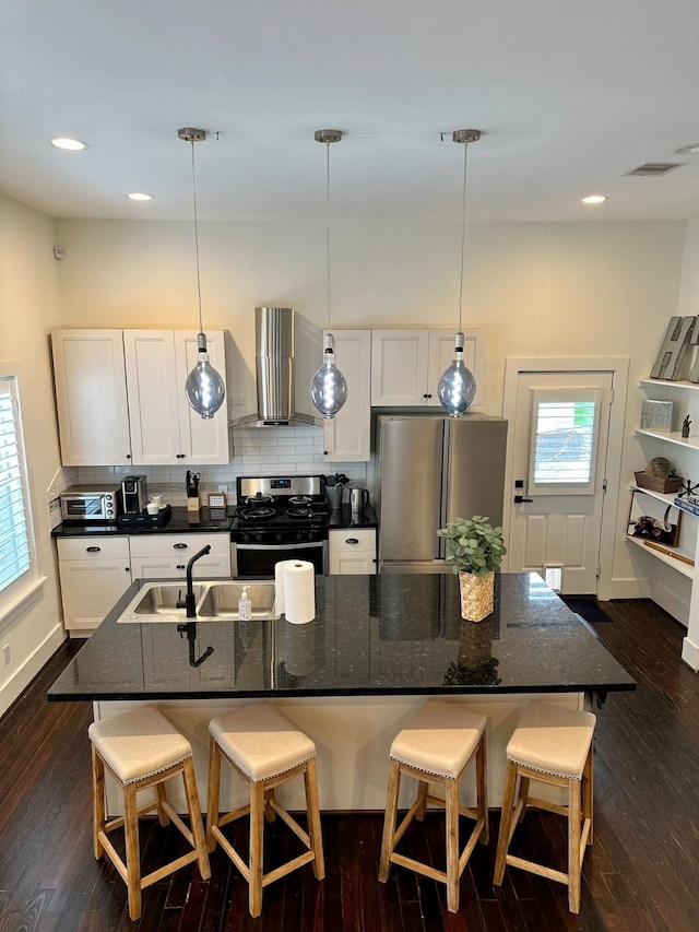 kitchen with a breakfast bar, dark wood-type flooring, wall chimney exhaust hood, appliances with stainless steel finishes, and decorative light fixtures