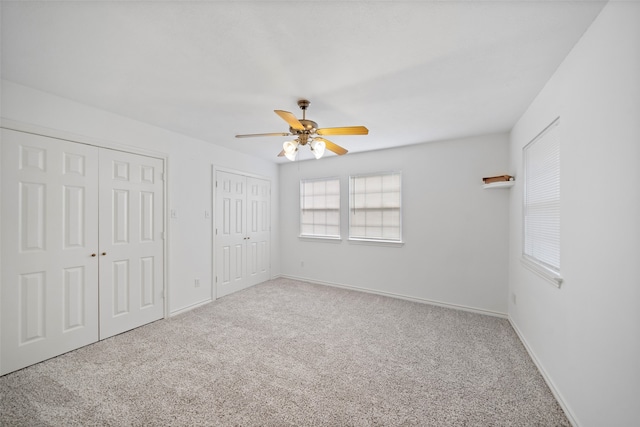 unfurnished bedroom with ceiling fan, light carpet, and two closets