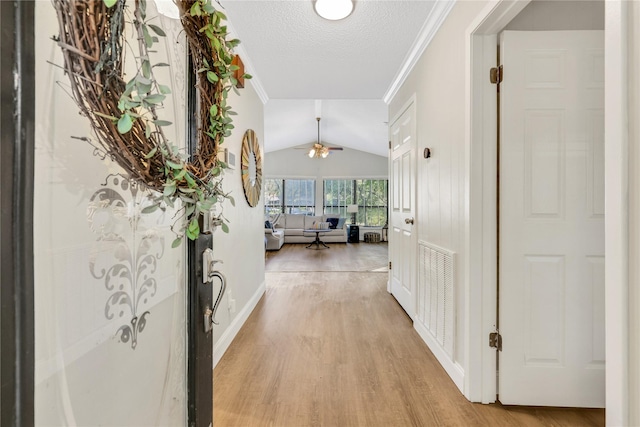 hall featuring light wood-type flooring, visible vents, lofted ceiling, and crown molding