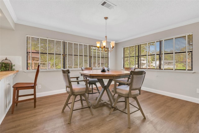 dining area featuring crown molding, light wood-style flooring, a notable chandelier, and visible vents