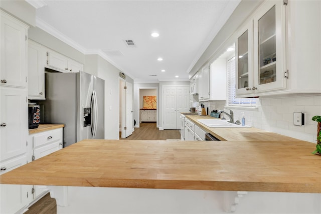 kitchen featuring visible vents, ornamental molding, stainless steel refrigerator with ice dispenser, a sink, and wood counters