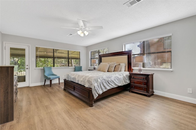 bedroom featuring light wood finished floors, visible vents, a textured ceiling, and baseboards