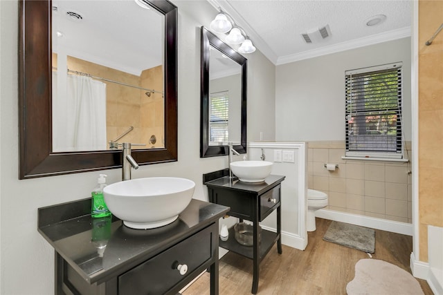 bathroom with wood finished floors, visible vents, ornamental molding, a textured ceiling, and tile walls