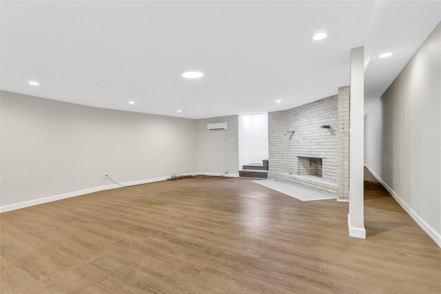 unfurnished living room with a wall mounted air conditioner, light wood-style flooring, recessed lighting, baseboards, and a brick fireplace