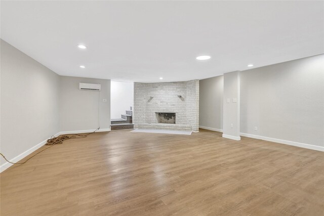 unfurnished living room featuring an AC wall unit, recessed lighting, a fireplace, light wood finished floors, and baseboards