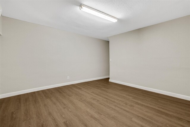 unfurnished room with a textured ceiling, baseboards, and wood finished floors