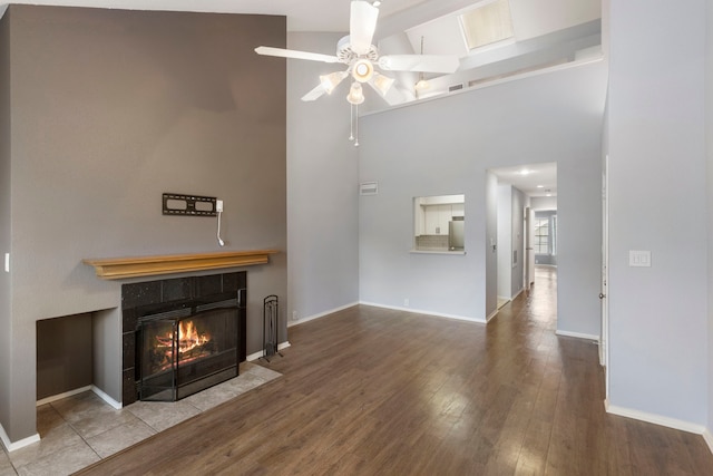 unfurnished living room featuring ceiling fan, a tile fireplace, wood-type flooring, and high vaulted ceiling