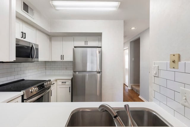 kitchen with decorative backsplash, stainless steel appliances, sink, hardwood / wood-style flooring, and white cabinetry