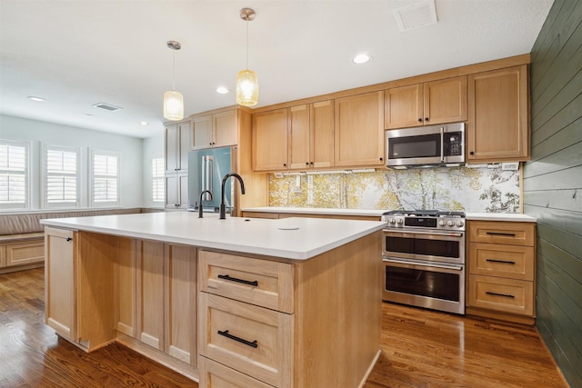 kitchen featuring hanging light fixtures, wood walls, an island with sink, wood-type flooring, and high end appliances