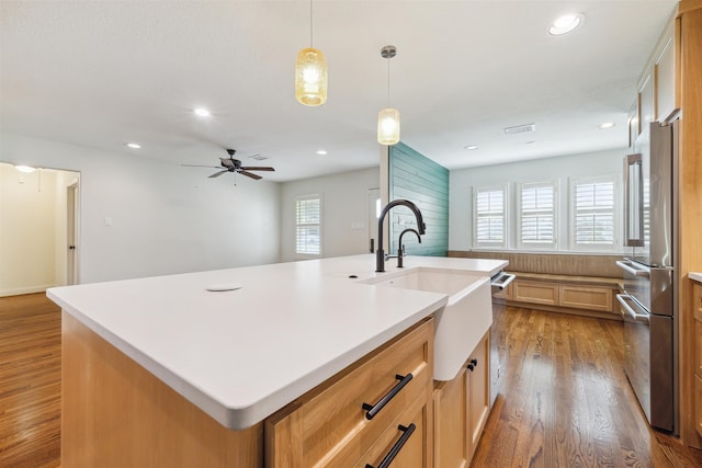 kitchen featuring high end refrigerator, a center island with sink, hanging light fixtures, and light hardwood / wood-style flooring