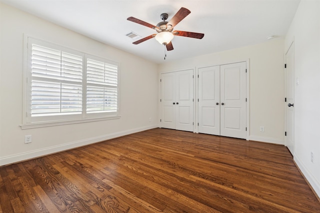 unfurnished bedroom featuring dark hardwood / wood-style flooring, two closets, and ceiling fan