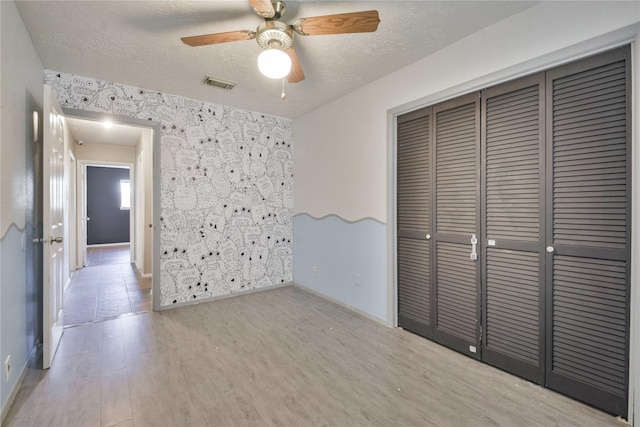 unfurnished bedroom featuring light wood-type flooring, a textured ceiling, a closet, and ceiling fan