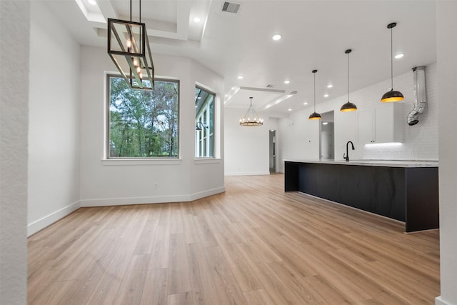 unfurnished living room with light hardwood / wood-style floors, a notable chandelier, and sink