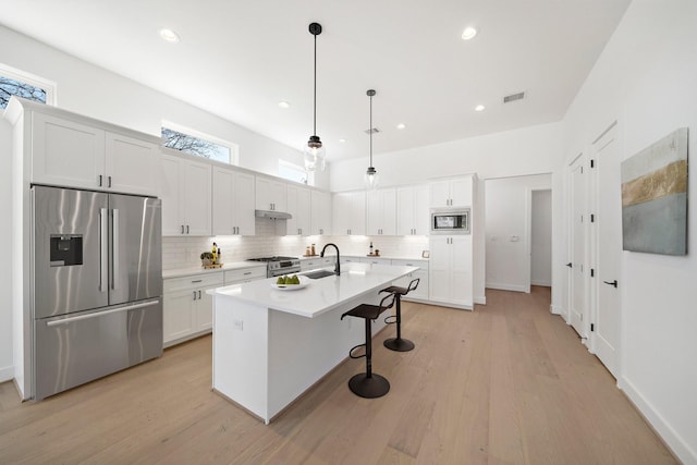 kitchen featuring appliances with stainless steel finishes, sink, pendant lighting, a center island with sink, and white cabinets