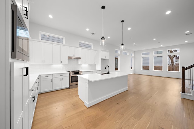 kitchen featuring stainless steel gas range, sink, pendant lighting, a kitchen island with sink, and white cabinets