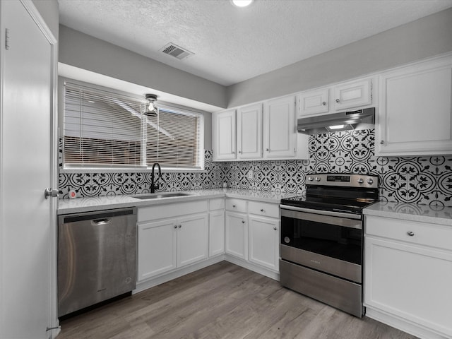 kitchen featuring appliances with stainless steel finishes, light wood-type flooring, tasteful backsplash, sink, and white cabinets